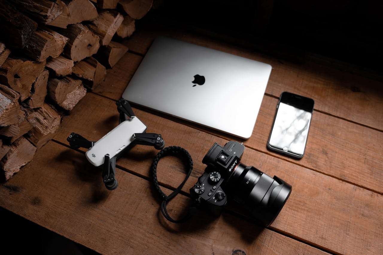ours-journey A flat lay of modern technology devices including a laptop, camera, drone, and smartphone on a wooden table.